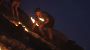 Eine Person auf einem steilen Hang platziert oder bewegt brennende Fackeln in der Nacht.