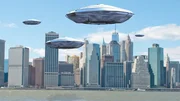 Mehrere fliegende Untertassen schweben &uuml;ber der Skyline einer gro&szlig;en Stadt am Wasser.