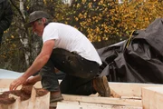 Maciah kniet sich bei der Arbeit auf dem Dach seiner neuen H&uuml;tte hin.