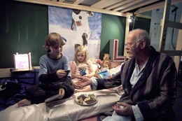 Opa Hubert (Joost Siedhoff, r.) huscht bei Leni (Paula Hartmann, M.) und Timmy (Max Schmuckert, l.) hinein und reicht ihnen nach dem ausgefallenen Abendbrot einen Teller mit Brot und Obst. Timmy und Hubert machen einen Deal aus: Timmy bekommt Nachhilfe in Mathe und erkl&auml;rt im Gegenzug seinem Opa das Wunder Handy.