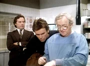 Bannister (Michael W. Goodwin, l.) und MacGyver (Richard Dean Anderson, M.) beobachten, wie der Pathologe (Arthur Malet, r.) eine Gewebeprobe entnimmt.