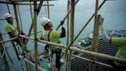 Tsim Sha Tsui, Hongkong: Zehn Meter lange Bambusstangen werden von den erfahrenen Ingenieuren von Hand &uuml;bergeben. Sie sind mit starken, aber flexiblen Nylonstr&auml;ngen verbunden. Die Flexibilit&auml;t des Bambus und der F&auml;den erlaubt es dem Bambusger&uuml;st, selbst die st&auml;rkeren Taifune in Hongkong zu &uuml;berleben.