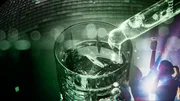 Aus einer kleinen Glasampulle fließt klare Flüssigkeit in ein mit Eiswürfeln und klarer Flüssigkeit gefülltes Glas. Auf der Seite tanzen Frauen, oben scheint eine überdimensionierte Disko-Kugel. Aus einer kleinen Glasampulle fließt klare Flüssigkeit in ein mit Eiswürfeln und klarer Flüssigkeit gefülltes Glas. Auf der Seite tanzen Frauen, oben scheint eine überdimensionierte Disko-Kugel.