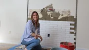 Leslie poses with tile in front of the in-progress fireplace backdrop