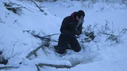 Kyle kneels in the snow surrounded by branches and sticks.