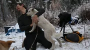 Behind the scenes of a crew member being loved on by a white dog in the snow. Behind the scenes of a crew member being loved on by a white dog in the snow.
