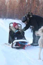 Ashley and Sydney Selden in the dogsled; Tyler Selden bent over talking to them. Ashley and Sydney Selden in the dogsled; Tyler Selden bent over talking to them.