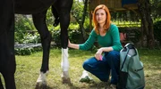 Zwei Frauen f&uuml;r alle Felle - Standfoto Film 3 "Pferdeliebe" Dr. med. Vet. Julia Kramer (Meriel Hinsching) untersucht das verletzte Pferd im Garten der Praxis.