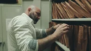 Ein Mann durchsucht Polizeiakten auf einem Regal im Archivraum.