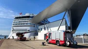 A firetruck at the cruise ship terminal Warnemünde. The turntable fire escape is extended to a window of the terminal. Behind the terminal lies a cruise ship. A firetruck at the cruise ship terminal Warnemünde. The turntable fire escape is extended to a window of the terminal. Behind the terminal lies a cruise ship.