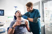 Dr. Mikko Rantala (Luan Gummich, r.) behandelt die Nase des Patienten Rick Schmitt (Ferdinand Seebacher, l.).
