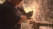 Funken fliegen, wenn der Teilnehmer das gl&uuml;hende Metall mit einem Flexodrucker schneidet.