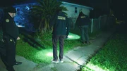 Mordermittler untersuchen den Hof in der Nacht mit Hilfe von Taschenlampen.
