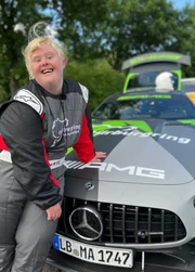 Angela lehnt im Rennanzug an einem Rennwagen.