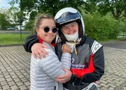 Angela umarmt in Rennanzug und mit Schutzhelm Giuliana, die sich nicht traut, mitzufahren (v.l.n.r. Giuliana, Angela).