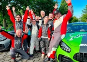 Die Gruppe steht nach der Rennfahrt mit den Rennfahrern am N&uuml;rburgring und jubelt.