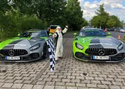 Patrick steht, die Startfahne hissend, zwischen zwei Rennautos.