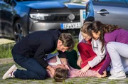 Tessa Schneider (Nell Pietrzyk, liegend) bricht auf dem Parkplatz vor ihrem Mann Dominik (Merlin Leonhardt, l.) zusammen, der sie gegen den &auml;rztlichen Rat von Dr. Elly Winter (Juliane Fisch, 2.v.r. mit Leslie-Vanessa Lill, r.) mit nach Hause nehmen wollte.