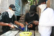 Ort: Kingston, Jamaika: 3 Dealer mit Kopft&uuml;chern sitzen um einen Tisch und laden ihre Waffen.
