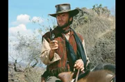 S&ouml;ldner Hogan (Clint Eastwood) reitet allzeit bereit durch die mexikanische W&uuml;ste und droht drei M&auml;nnern, die eine Frau bedr&auml;ngen, mit seinem Revolver.