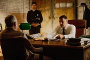 Der H&auml;ftling und der Inspektor sitzen am Tisch, w&auml;hrend der Polizist steht.