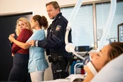 Ria Wilms (Maike Bollow) wird von Ella (Ines Quermann) und Polizist Chris Friedrichs (Oliver Clemens) aus dem Krankenzimmer gef&uuml;hrt. Die Patientin Annika Wilms (Luisa Schmidt) liegt regungslos in ihrem Bett.