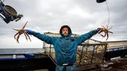 Northwestern deckhand Karl Rasmussen posing holding baridi crab, pot in the background
