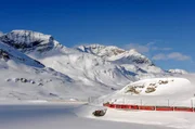 Der Bernina Express auf dem Berninapass am Lago Bianco: Der Zug schl&auml;ngelt sich durch tiefe T&auml;ler, wilde Schluchten und &uuml;ber das ewige Eis der B&uuml;ndner Alpen.