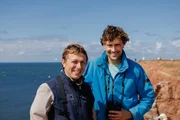 Uli Kunz und Umweltsch&uuml;tzer Elmar Ballstaedt stehen gemeinsam auf dem Lummenfelsen auf Helgoland. Im Hintergrund nisten die Basst&ouml;lpel.