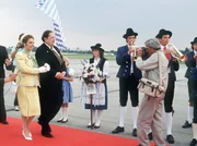 Standesgem&auml;&szlig; wird die K&ouml;nigin von Mandalia (Michaela May, l.) vom Ministerpr&auml;sidenten (Georg Marischka) auf dem Flughafen in Empfang genommen. Herbie (Dieter Hildebrandt, r.) ist dabei voll in Aktion.