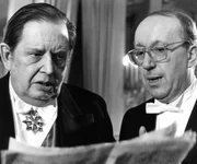 &Uuml;ber die Berichterstattung von Baby Schimmerlos zum Staatsbesuch der K&ouml;niglichen Hoheit ist der Ministerpr&auml;sident (Georg Marischka, links) emp&ouml;rt. Staatssekret&auml;r Klaustaler (Walter Schmiedinger) soll da die geeigneten Gegenmassnahmen einleiten.