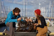 Uli Kunz und WWF-Mitarbeiterin Gabrielle Dederer sitzen am Olympiahafen in Schilksee. Sie haben ein Geisternetz in der Hand, welches sie aus der Ostsee geholt haben.