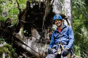 Uli Kunz sitzt mit Schutzhelm und Kletterausr&uuml;stung auf einem Baumstamm im rum&auml;nischen Wald.