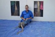 Robert sitzt vollkommen still mit einer Klapperschlange auf dem Kopf und einer weiteren auf den Beinen.