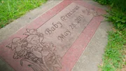 Eine Steinplatte auf einer Wiese zeigt die Inschrift &bdquo;Baby Precious &ndash; May 28, 2013&ldquo; mit gravierten Engeln und Blumen.