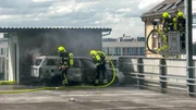 Feuerwehrleute l&ouml;schen ein brennendes Auto.