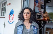 Yeliz Bulut (Ariella Hirshfeld), die Chefin von &bdquo;Delivery Ape&ldquo; beobachtet mit ernstem Blick den Disput zwischen Adrian und Pablo.