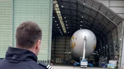 Techniker und Ingenieure arbeiten zwischen Handarbeit und Hightech an einem Luftschiff, das &uuml;ber 120 Jahre Zeppelin-Geschichte fortf&uuml;hrt.