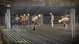 Auf der Baustelle im Inneren des Hochhauses verlegen Bauarbeiter millimetergenau tonnenschwere Stahlarmierungen.