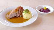 Hauptgericht des Augustiner am W&ouml;rthsee - Viertel bayrische Ente vom Lugederhof mit Kartoffelkn&ouml;del und Apfelblaukraut - wird in wei&szlig;em Geschirr auf einem Tisch pr&auml;sentiert.