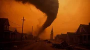 Ein Tornado zieht durch eine verlassene Stra&szlig;e mit H&auml;usern und einer Kirche im Hintergrund.