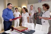 Hans-Peter Brenner (Michael Trischan, links) hat seinen ersten Tag des "Praktischen Jahres". Allen f&auml;llt der Abschied schwer. Doch seine Kollegen haben ein tolles Abschiedsgeschenk, das ihm den Wechsel ins &Auml;rzteteam erleichtern soll.  Von links: Hans-Peter Brenner (Michael Trischan), Kris Haas (Jascha Rust), Arzu Ritter (Arzu Bazman), zwei Komparsen, Ulrike Stolze (Anita Vulesica).