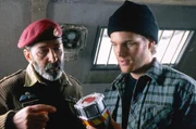 Colonel Amir Salim (Roshan Seth, l.) erkl&auml;rt Peter Garrett (Chris O&rsquo;Donnell, r.) worauf er beim Umgang mit dem Sprengstoff achten muss.