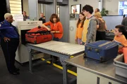 Als Frankie (Patricia Heaton, 2.v.l.) ihren Koffer heillos &uuml;berpackt, m&uuml;ssen sich Sue (Eden Sher, 3.v.l.), Axl (Charlie McDermott, 2.v.r.) und Brick (Atticus Shaffer, r.) im wahrsten Sinne des Wortes warm anziehen, um von der Sicherheitsbeamten (Luenell Campbell, l.) durchgelassen zu werden ...