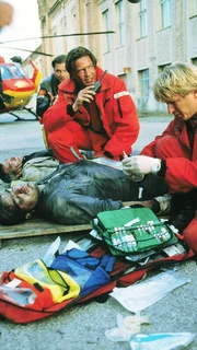 Dr. Michael L&uuml;dwitz (Rainer Grenkowitz, M.) und der Sanit&auml;ter Peter Berger (Serge Falck, r.) k&uuml;mmern sich um verletzte Arbeiter (Komparsen), die Opfer einer Bombenexplosion wurden.