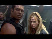 Teal'c (Christopher Judge, li.) und Ishta (Jolene Blalock, re.) treffen sich auf einem Planeten mit einem Informanten...