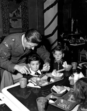 &Uuml;ber 30 Kindergarten-Kinder der Schule Schwarzstrasse zu Gast bei der Weihnachtsfeier; M/Sgt Charles L. Shriner hilft einem Kind beim Fleischschneiden.
