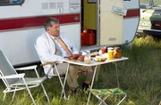 Dr. Rufus Kloppstedt (Veit St&uuml;bner) hat seinen Wohnwagen auf der gro&szlig;en Dorfwiese abgestellt und genie&szlig;t sein Fr&uuml;hst&uuml;ck (Szene aus 'Neues aus B&uuml;ttenwarder').