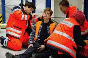 Christian (Francis Fulton-Smith, l.) ist als Notarzt vor Ort: Boris Kehr (J&uuml;rgen Klein, M.) wurde von einer herabfallenden Pallette verletzt (mit Komparsen, r.).