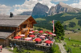 Beliebter Rastplatz in den Dolomiten im Norden Italiens: Auf der Seiseralm ist die Terrasse der Rauchh&uuml;tte gut besucht. Im Hintergrund Langkofel und Plattkofel.